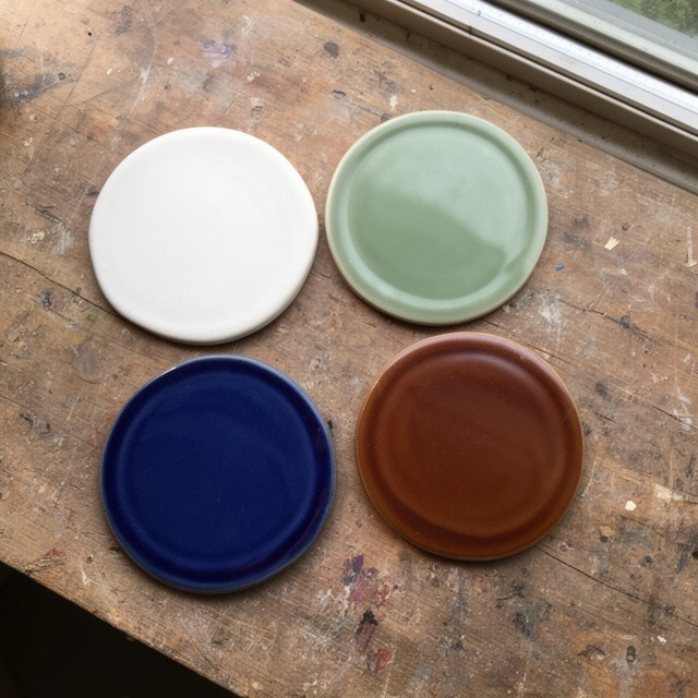 Four stoneware sample tiles in white, green, blue and brown on a wooden table