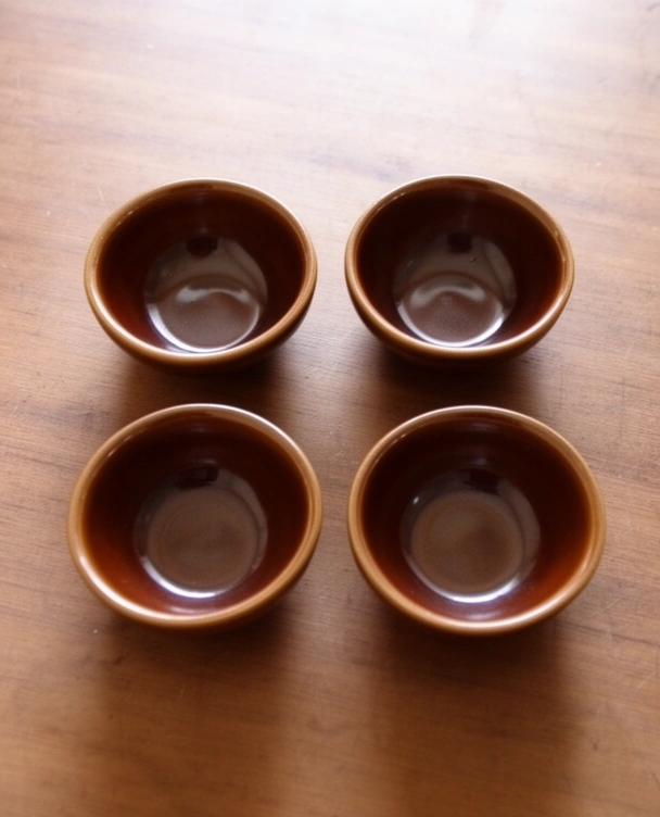 Four empty brown glazed katoris on a wooden table