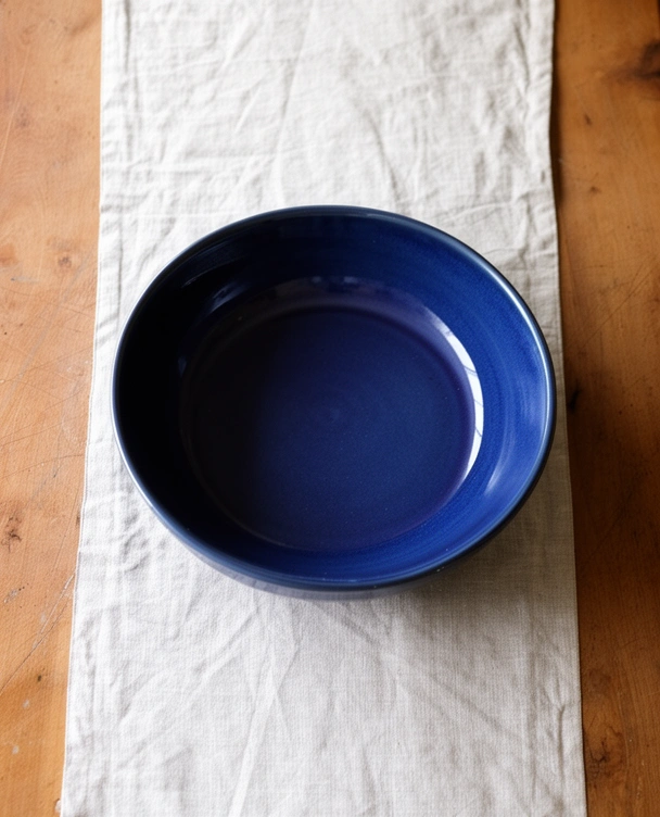 Empty deep blue glazed serving bowl on a linen table runner